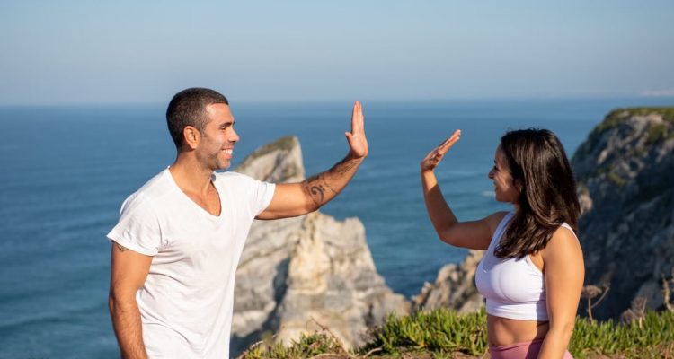 Fit couple in athletic wear high-fiving by the sea on a sunny day in Portugal.